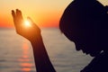 Silhouette of young woman raising hands praying at sunset or sunrise light