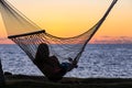 Silhouette of a young woman resting in a hammock and watching sunset over Pacific ocean