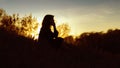 Silhouette of a young woman sitting on a hill at sunset, figure of girl in the autumn landscape