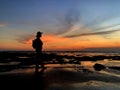 Silhouette of a young woman with a smile and a bag standing alone watching sunset in the beach. Peaceful feeling, self healing