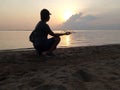 Silhouette of young woman smile and squat down, hand holding a fishing boat floating in the sea on soft light of sunrise Royalty Free Stock Photo