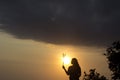 Silhouette of a young woman standing alone, holding grass flower in hand on golden sunset light sky background. Royalty Free Stock Photo