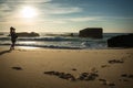 Silhouette of young woman standing on scenic sandy beach taking photos of beautiful seascape of atlantic ocean with waves in sunny Royalty Free Stock Photo