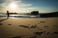 Silhouette of young woman standing on scenic sandy beach taking photos of beautiful seascape of atlantic ocean with waves in sunny