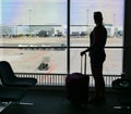 SILHOUETTE: Young woman stands by the window and looks at the airport runway. Royalty Free Stock Photo