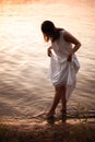 the silhouette of a young woman in a summer white dress walking along the edge of cool water on the beach by the river Royalty Free Stock Photo