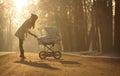 Silhouette of young woman on sunny footpath and looking at child in baby stroller. Sunny winter park, childcare and love Royalty Free Stock Photo