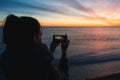 Silhouette of a young woman taking a photo of a sunset with her smartphone.