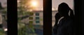 Silhouette Of Woman Talking On Mobile Phone While Standing Near Window With View On Sunset In City.
