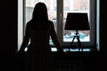 Silhouette of a young woman at the window. Vintage lamp on the windowsill Royalty Free Stock Photo