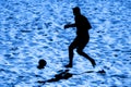 Silhouetted beach soccer action of male player on sand.Blue color filter