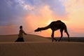 Silhouetted bedouin walking with his camel at sunset, Thar desert near Jaisalmer, India