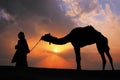 Silhouetted bedouin walking with his camel at sunset, Thar desert near Jaisalmer, India