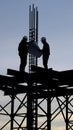 Silhouetted construction workers in hard hats study blueprints atop a steel structure against a twilight sky Royalty Free Stock Photo