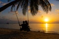 Silhouetted couple in love walks on the beach during sunset. Riding on a swing tied to a palm tree and watching the sun go down Royalty Free Stock Photo