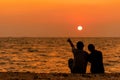 Silhouetted couple sitting, and relax on beach in love and embrace, sunset in the beach. Royalty Free Stock Photo