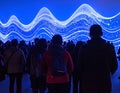 Silhouetted Crowd Engaged by Dynamic Blue Light Wave Art Installation Royalty Free Stock Photo