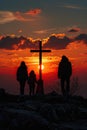 Silhouetted family at sunset with a cross on a rocky hill.