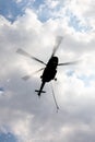 Silhouetted flying helicopter with sling with overcast sky