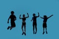 Silhouetted full length shot of four little sportive kids looking joyful while posing, jumping isolated over blue