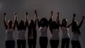 Silhouetted group of diverse women holding, raising their arms together while standing over grey background. Diversity