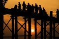 Silhouetted people crossing U bein bridge with sunset.