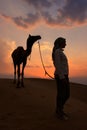 Silhouetted person with a camel at sunset, Thar desert near Jaisalmer, India