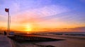 A silhouetted woman stands by the RNLI flag on Rhyl beach watching a stunning sunsetset