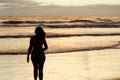 A silhouetted woman walking near the sea on a beach with the sun rising and the sunrays reflecting in the sea water. Royalty Free Stock Photo