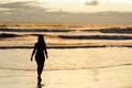 A silhouetted woman walking near the sea on a beach with the sun rising and the sunrays reflecting in the sea water. Royalty Free Stock Photo