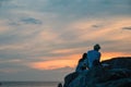 Silhouettes boy and girl at sunset over the tropical sea. Young man and girl sit on rock and look at seascape. Rear view. Royalty Free Stock Photo