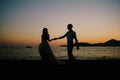 Silhouettes of the bride and groom holding hands walking along the beach at sunset Royalty Free Stock Photo