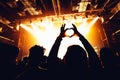 silhouettes of concert crowd in front of bright stage lights. People showing heart symbol. hands of audience making heart shaped h