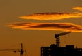 Silhouettes of construction cranes and construction on sunset sky background. Yellow hot clouds in the sky above Royalty Free Stock Photo