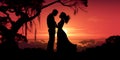 Silhouettes of couple in love who kissing against orange sunset at evening under tree Royalty Free Stock Photo