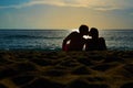 Silhouettes of a couple, man and woman sitting on a sandy beach and kissing with sunset on the sea on a background. Royalty Free Stock Photo