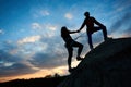 Woman with rope engaged in sports of rock climbing on the top of cliff. Her friend helping her