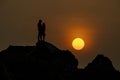 Silhouettes couple standing on rock at the beach with sunset on background.