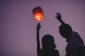 silhouettes of couple waving hands to flying chinese lantern in violet