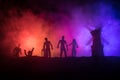 Silhouettes crowd of hungry zombies and old windmill on hill against dark foggy toned sky. Silhouettes of scary zombies walking at