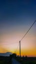 silhouettes of electric poles around the rice fields against the backdrop of mountains and a golden sunset Royalty Free Stock Photo