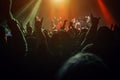 Silhouettes of enthusiastic fans with raised hands are illuminated by the beams of stage lights