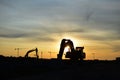 Silhouettes of excavators at a construction site against the background of tower cranes and sunset. Royalty Free Stock Photo