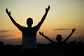 Silhouettes of father and daughter with hands up having fun, against sunset sky. Royalty Free Stock Photo