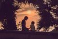 Silhouettes of the father and son, who meet the sunset in the tropics against the backdrop of palm trees