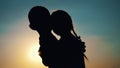 Silhouettes, figures of children, boy and girl, brother and sister hugging against the background of the sun, at sunset