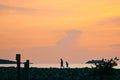 Silhouettes of a fisherman and a kid walking along the shore at sunset. Royalty Free Stock Photo