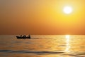 Silhouettes of fishermen against a bright sunset with a large yellow sun under the surface of the sea. Royalty Free Stock Photo