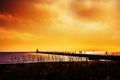 Silhouettes of fishermen on a long pier by the lighthouse. Royalty Free Stock Photo