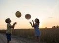 silhouettes of a girl and a boy of 6 years old, toss and catch hats against the backdrop of sunset Royalty Free Stock Photo